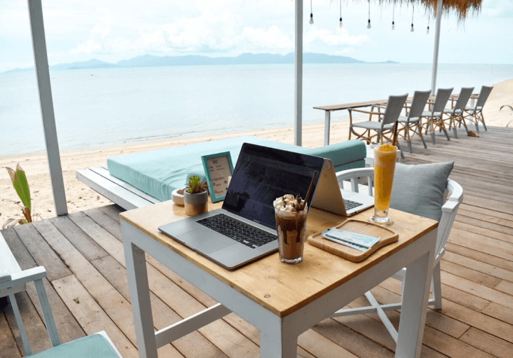A laptop sitting on a table by the beach.