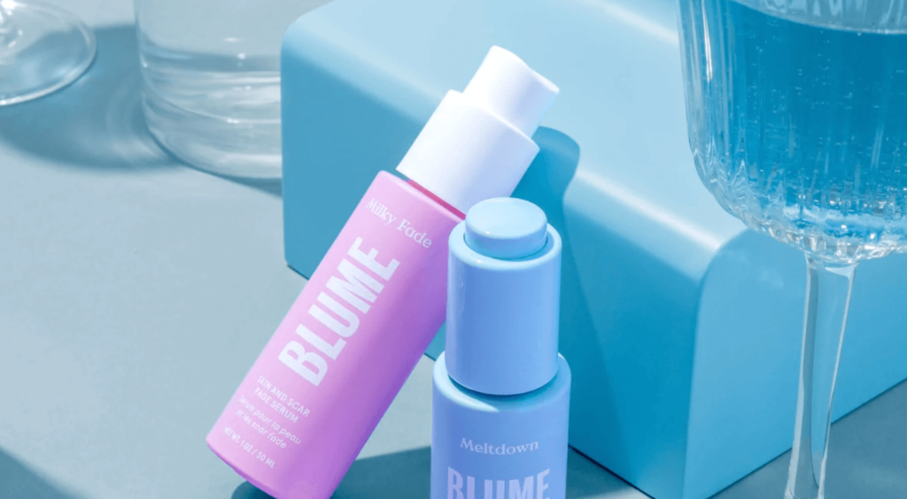 A pink bottle of product from Blume resting on a box with a blue bottle sitting next to it.