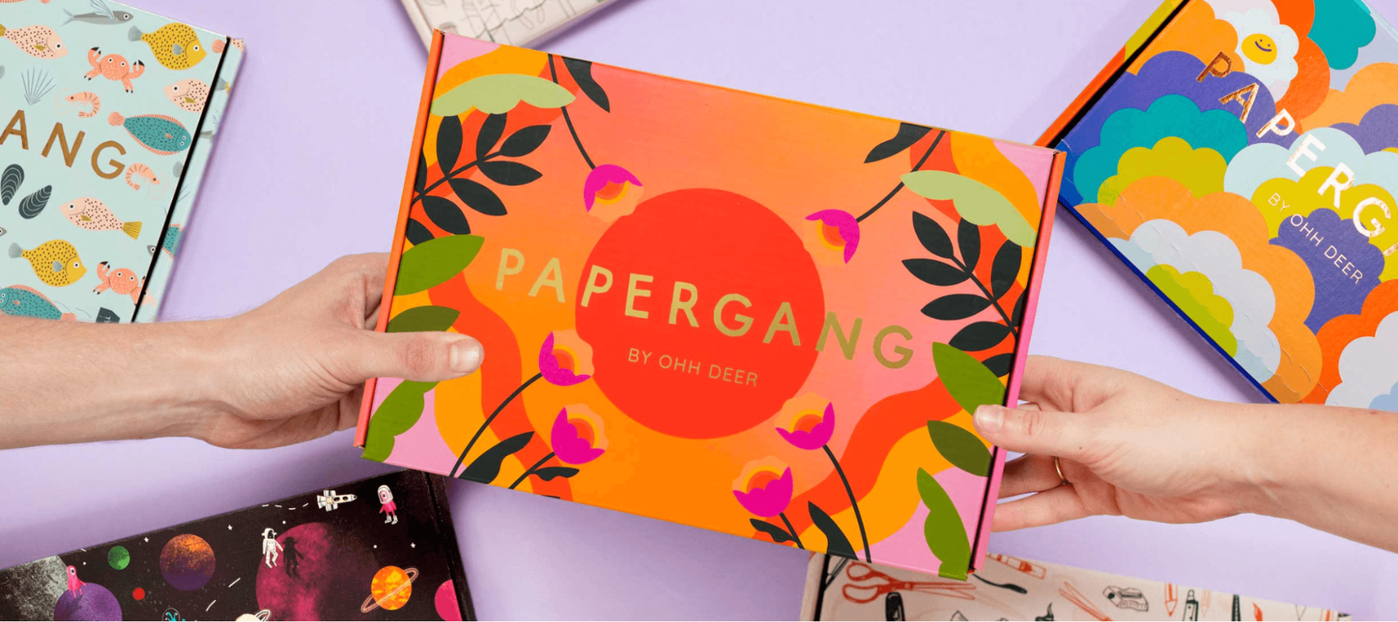 Two hands holding a box with the Papergang logo on it surrounded by other designed boxes on the table.